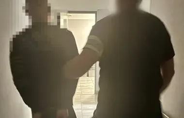 Dwie osoby w czarnych koszulkach stoją w wąskim korytarzu, w tle widoczne otwarte drzwi i podłoga z płytek.