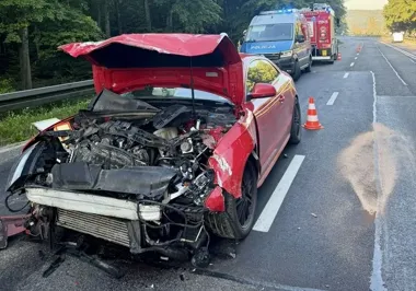 Czerwone auto osobowe z poważnie uszkodzoną przednią częścią stoi na jezdni przy udziale policji i straży pożarnej.